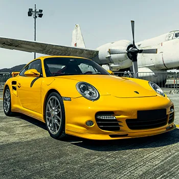 Yellow sports car near vintage airplane on runway.